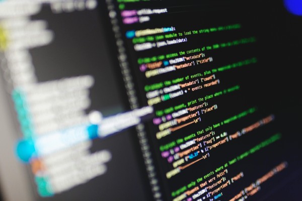 Computer screen displaying colorful HTML and CSS code with syntax highlighting, showing a professional web development environment with multiple lines of code in green, pink, and yellow text on a dark background